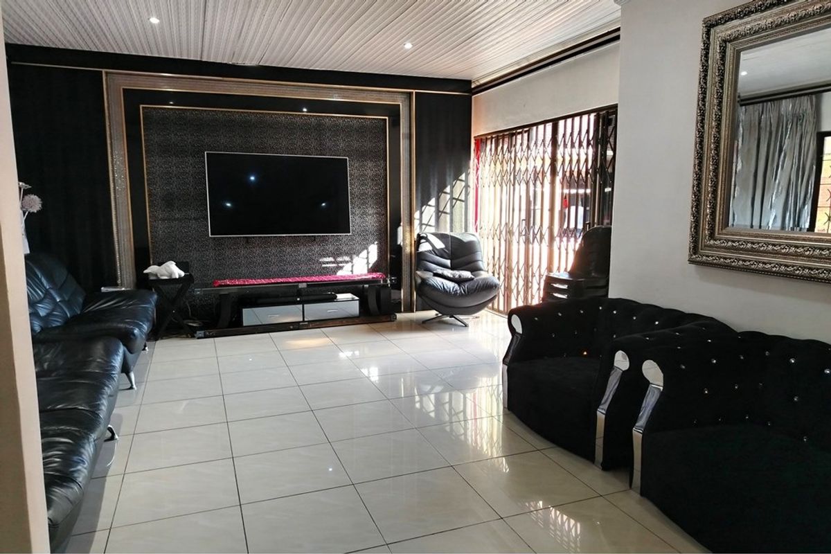 Spacious living room featuring large format floor tiles, a decorative feature wall with integrated lighting, and a security gate leading to the exterior.