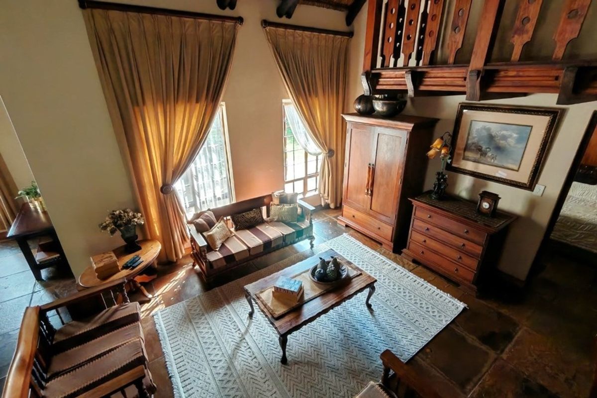 A spacious living room featuring high ceilings, exposed timber mezzanine railing, and traditional stone flooring, creating a warm and rustic atmosphere.