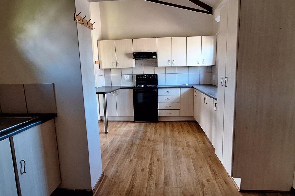 A functional kitchen featuring light-toned cabinetry, dark countertops, a built-in stove with extractor fan, and wood-look flooring.