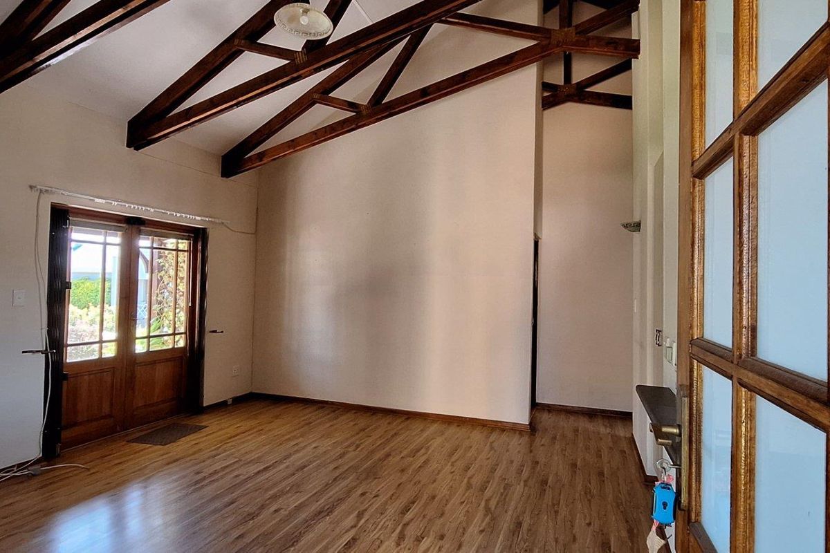Spacious living area featuring high vaulted ceilings with exposed timber trusses, laminate flooring, and double glass-paneled doors leading to the exterior.
