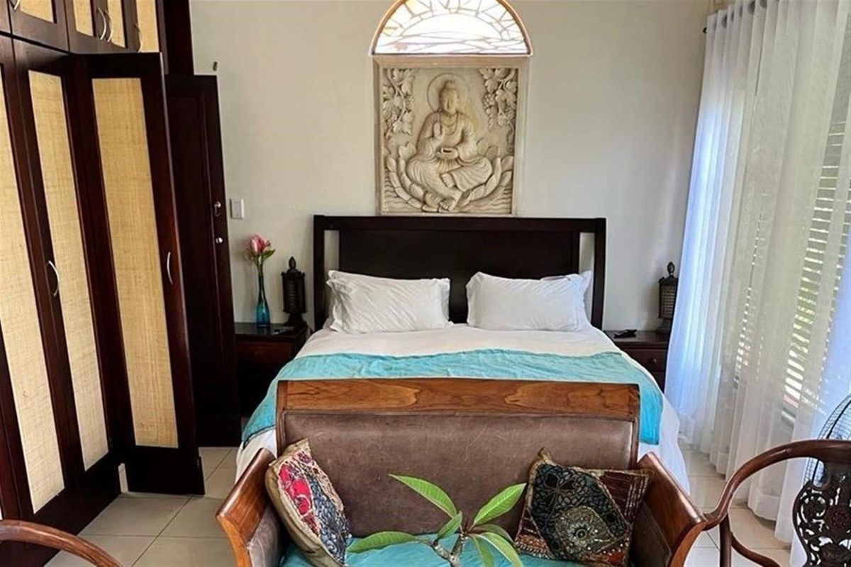 A well-maintained bedroom featuring built-in dark wood cabinetry, tiled flooring, and a decorative arched window detail above the bed area.