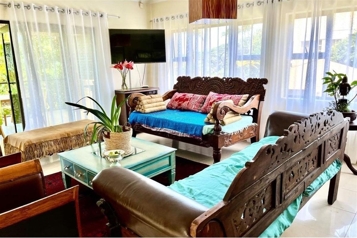 A bright living room featuring large windows with sheer curtains, tiled flooring, and a wall-mounted television.
