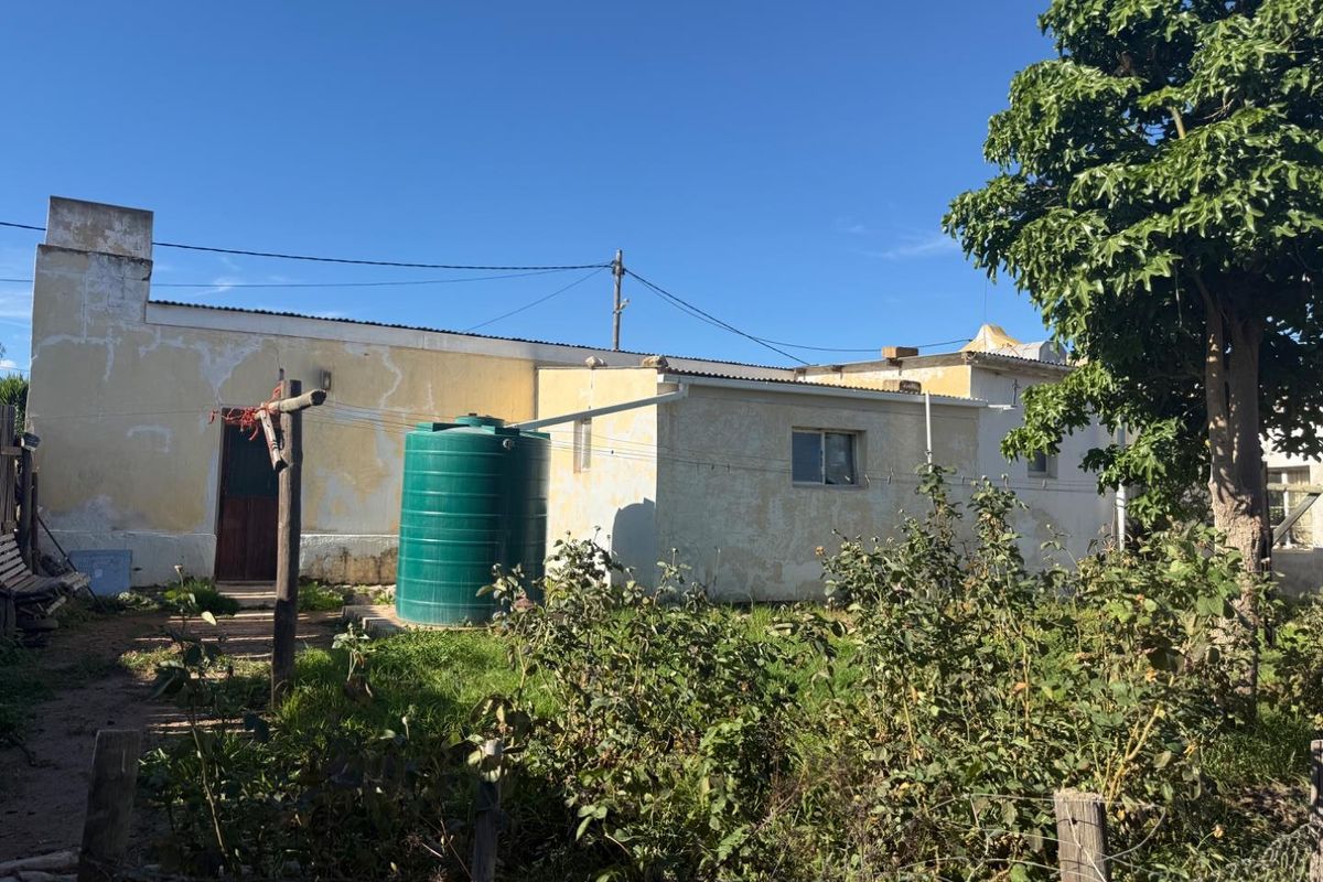 Rear view of the property showing the exterior wall, a water storage tank, and the garden area.