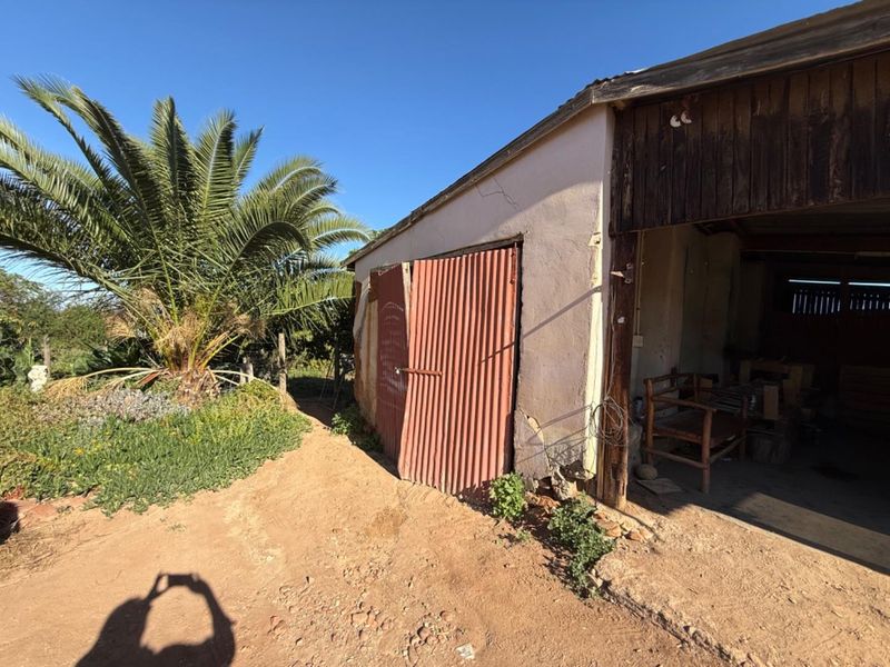 Exterior view of a weathered outbuilding or garage structure featuring corrugated metal doors and timber cladding, requiring significant maintenance and repair.