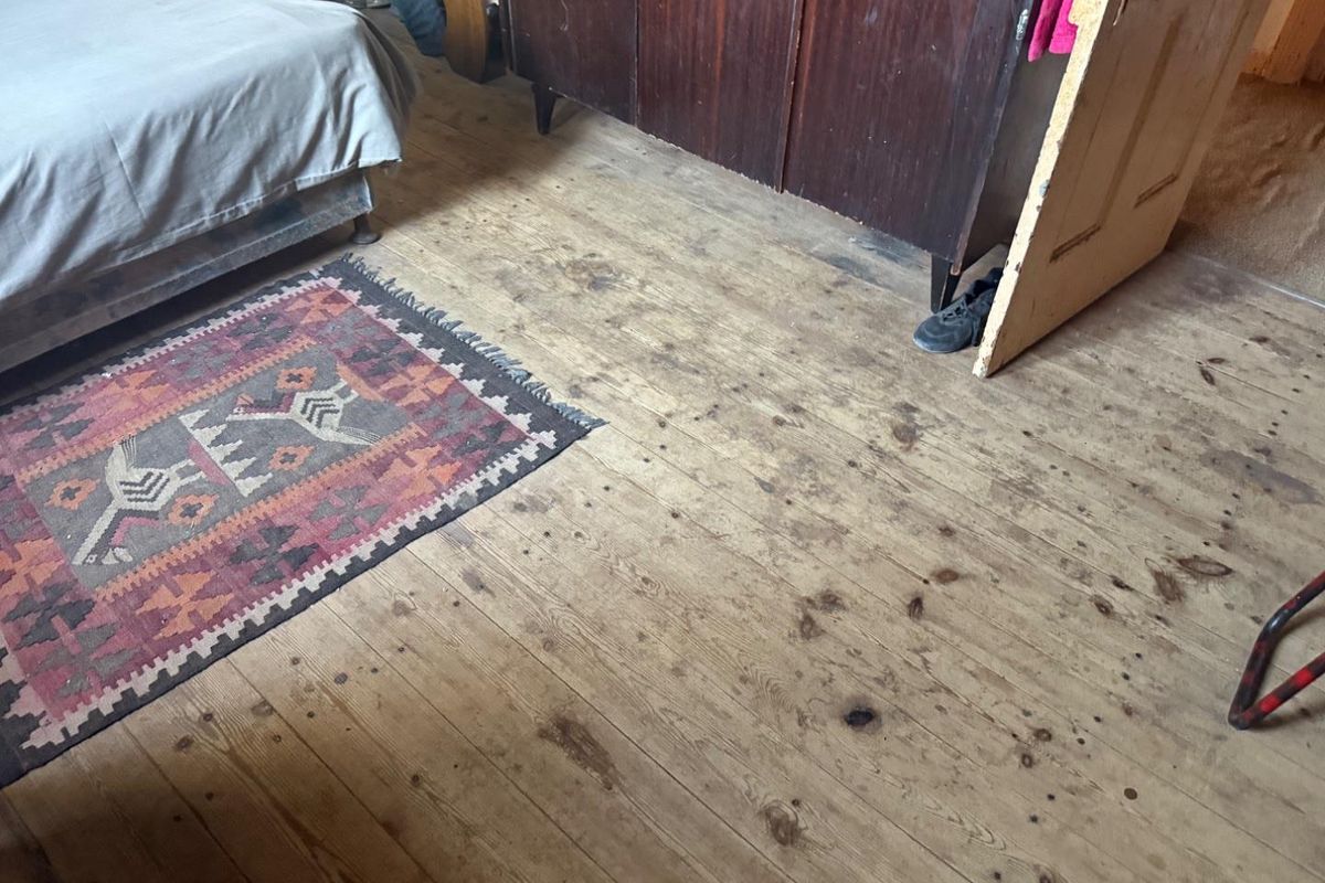 A bedroom featuring exposed timber floorboards and a traditional wooden door.