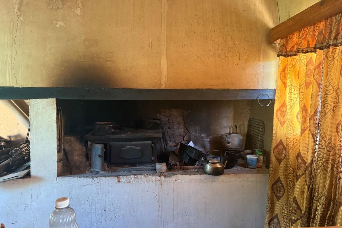A rustic indoor fireplace or hearth area featuring a built-in wood-burning stove, showing significant signs of wear and soot accumulation.