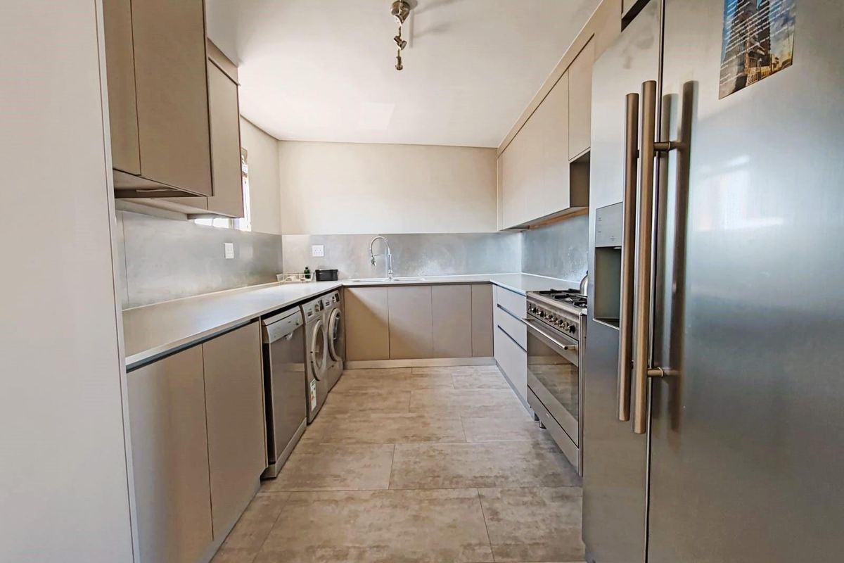 Modern galley-style kitchen featuring sleek cabinetry, stone countertops, stainless steel gas range, and integrated laundry appliances.