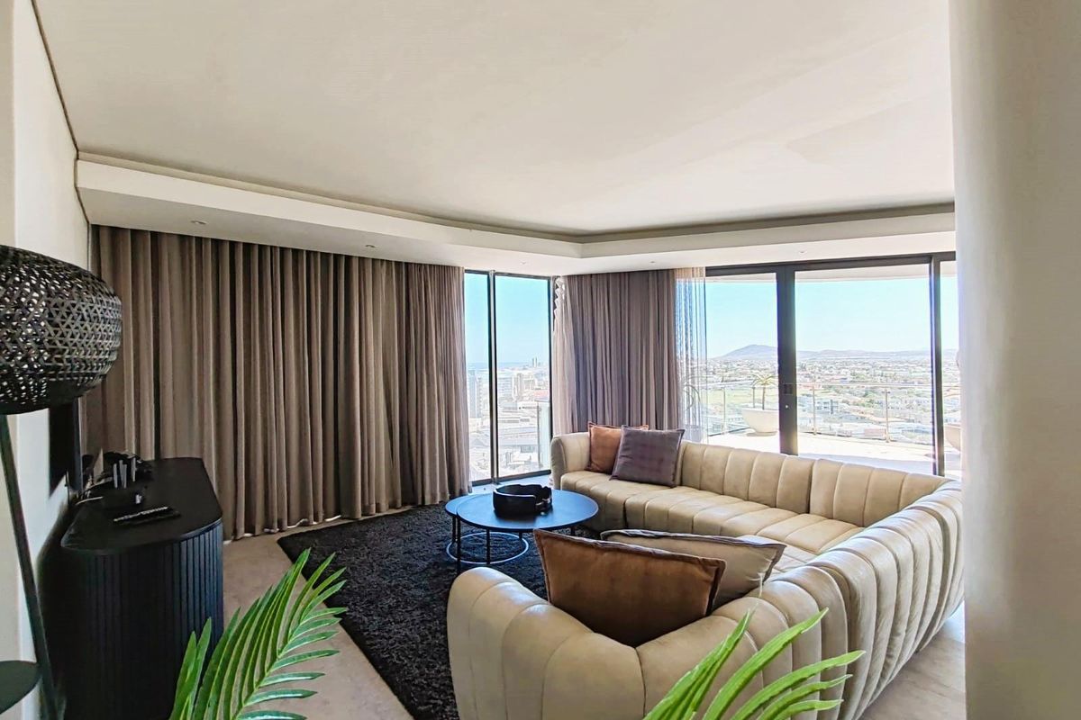 A bright, modern living room featuring floor-to-ceiling windows with expansive city views and access to a private balcony.