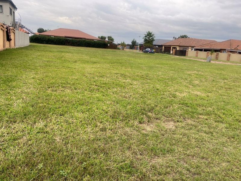 A vacant residential plot featuring a level grass lawn and established boundary walls in a developed neighborhood setting.