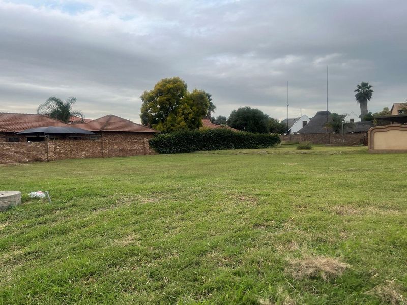 A vacant residential plot featuring a grassed area, enclosed by brick boundary walls, situated within an established residential neighborhood.