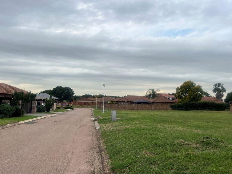 A view of the residential street frontage showing the paved road, grass verge, and surrounding neighborhood boundary walls.