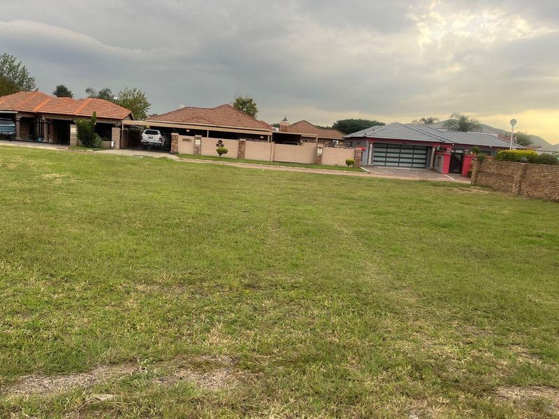 A vacant residential plot featuring a level grass lawn with established neighboring properties and boundary walls visible in the background.