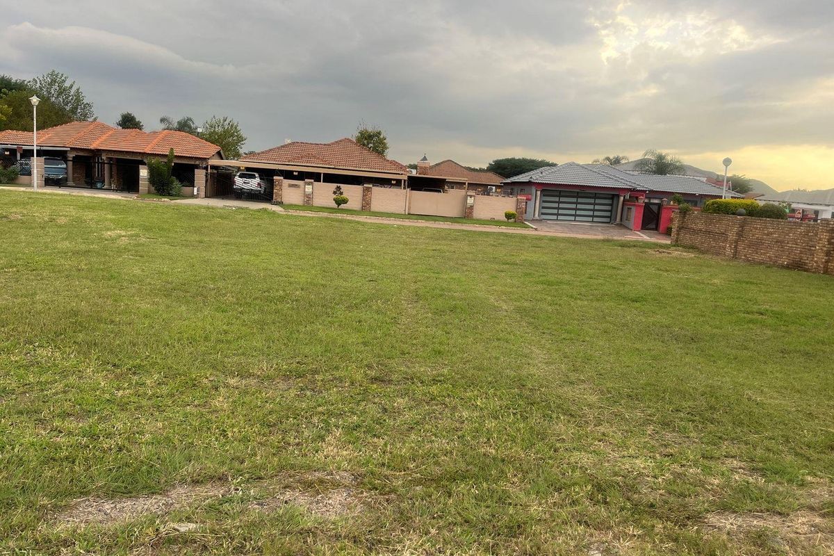 A vacant residential plot featuring a level grass lawn with established neighboring properties and boundary walls visible in the background.