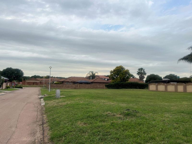 A vacant residential plot situated on a paved street, featuring established boundary walls and surrounding neighborhood infrastructure.
