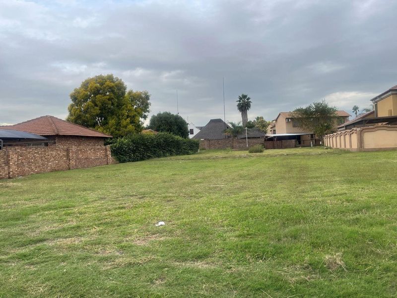 A view of a vacant residential plot featuring a grass lawn and established brick boundary walls.