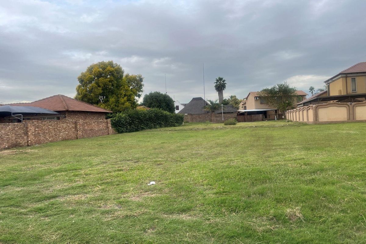 A view of a vacant residential plot featuring a grass lawn and established brick boundary walls.