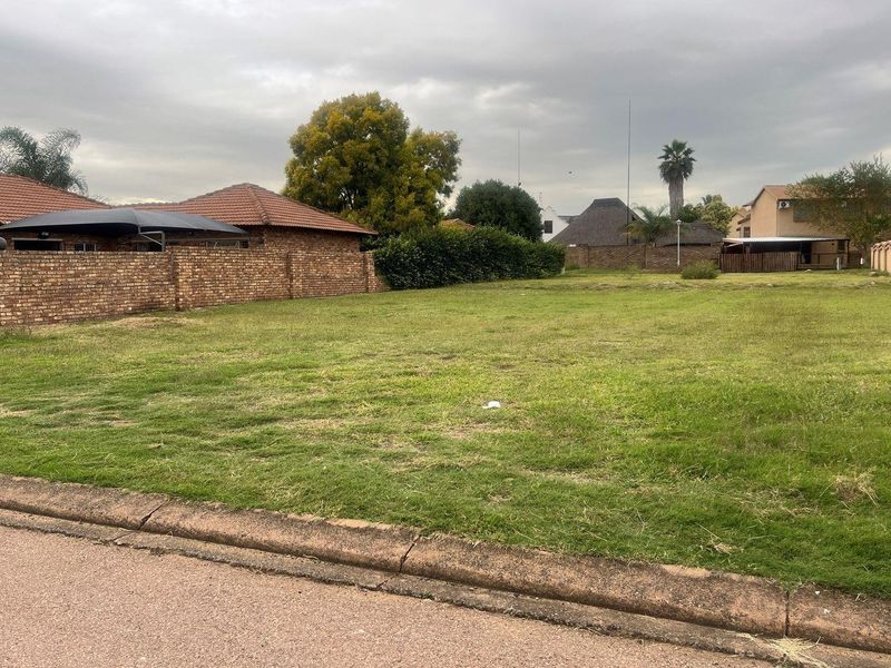 A vacant residential plot of land featuring a grassed surface, enclosed by brick boundary walls and accessible from the street.