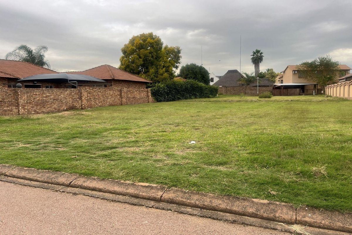 A vacant residential plot of land featuring a grassed surface, enclosed by brick boundary walls and accessible from the street.
