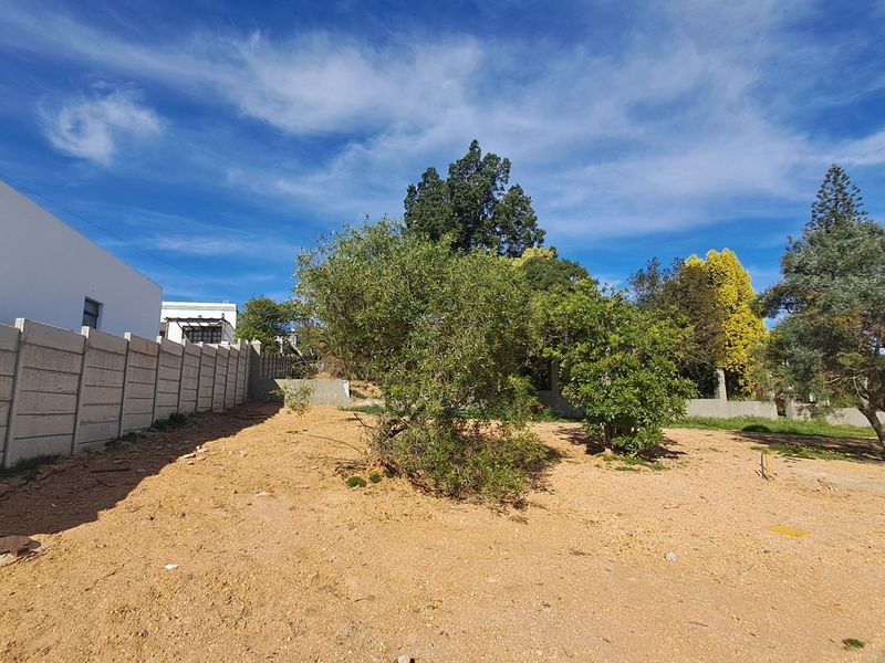 A vacant residential plot featuring a precast concrete boundary wall and established trees, offering a clear space for future development.