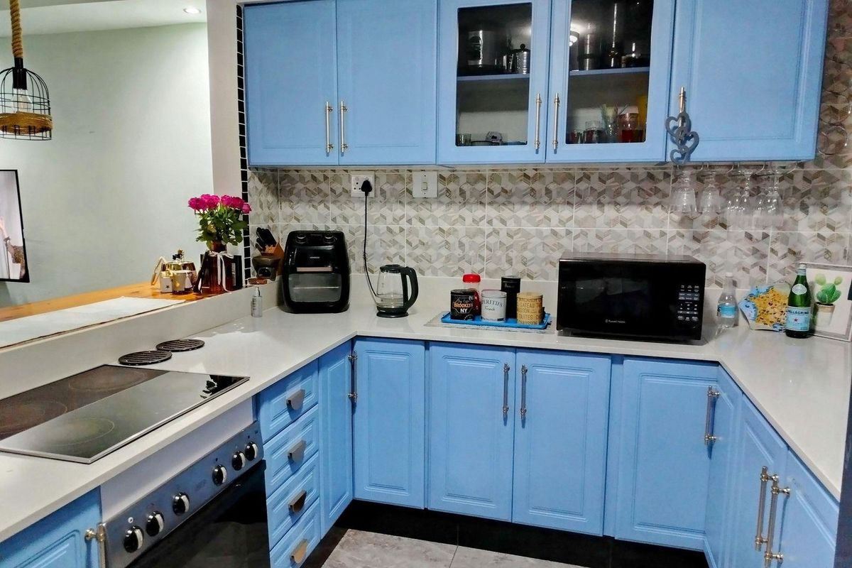 A well-maintained kitchen featuring light blue cabinetry, stone countertops, a modern electric hob, and a decorative tiled backsplash.