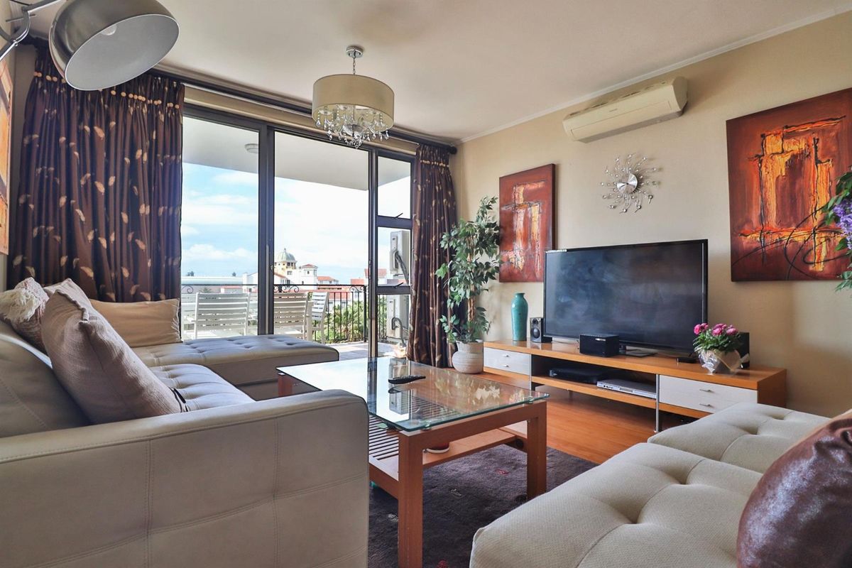 A comfortable living room featuring wood-look flooring, a wall-mounted air conditioning unit, and large sliding glass doors leading to a private balcony.