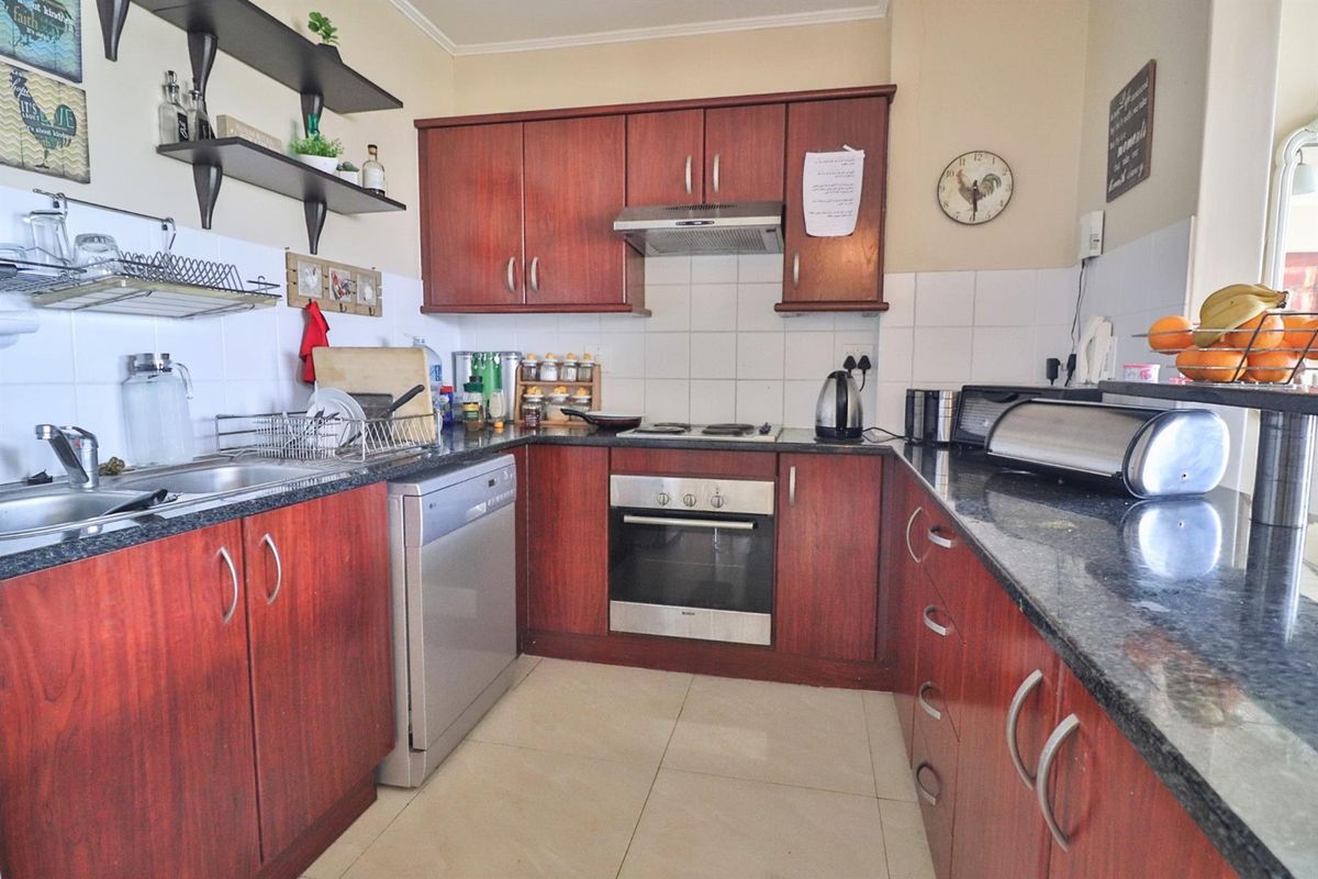 A functional U-shaped kitchen featuring dark wood cabinetry, granite countertops, a built-in oven, hob, and extractor fan with tiled flooring.