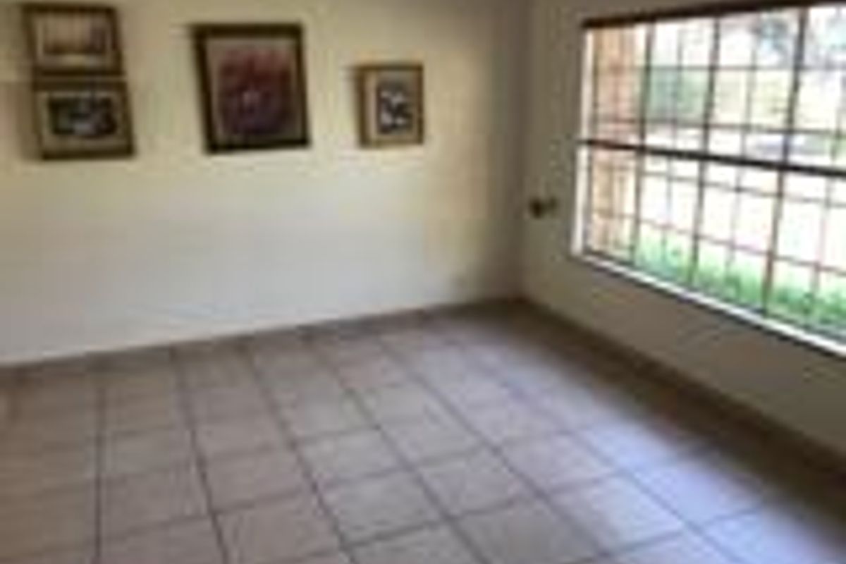 A bright living area featuring neutral ceramic floor tiles and a large window with security bars, offering a clean and functional space.