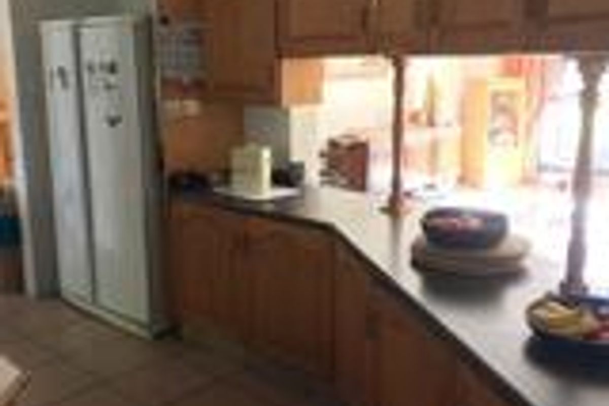 A dated kitchen featuring traditional timber cabinetry, laminate countertops, and tiled flooring, offering a functional layout with a breakfast bar pass-through.