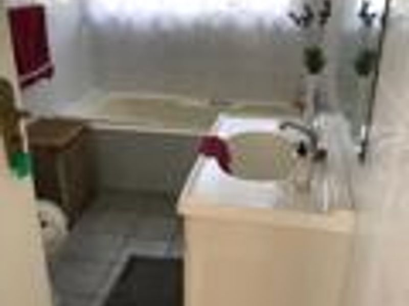 A compact bathroom featuring a built-in bathtub, vanity basin, and tiled flooring, requiring cosmetic updates to modernize the space.