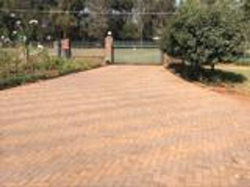 A paved driveway leading to a gated entrance with brick pillars, surrounded by established garden landscaping.