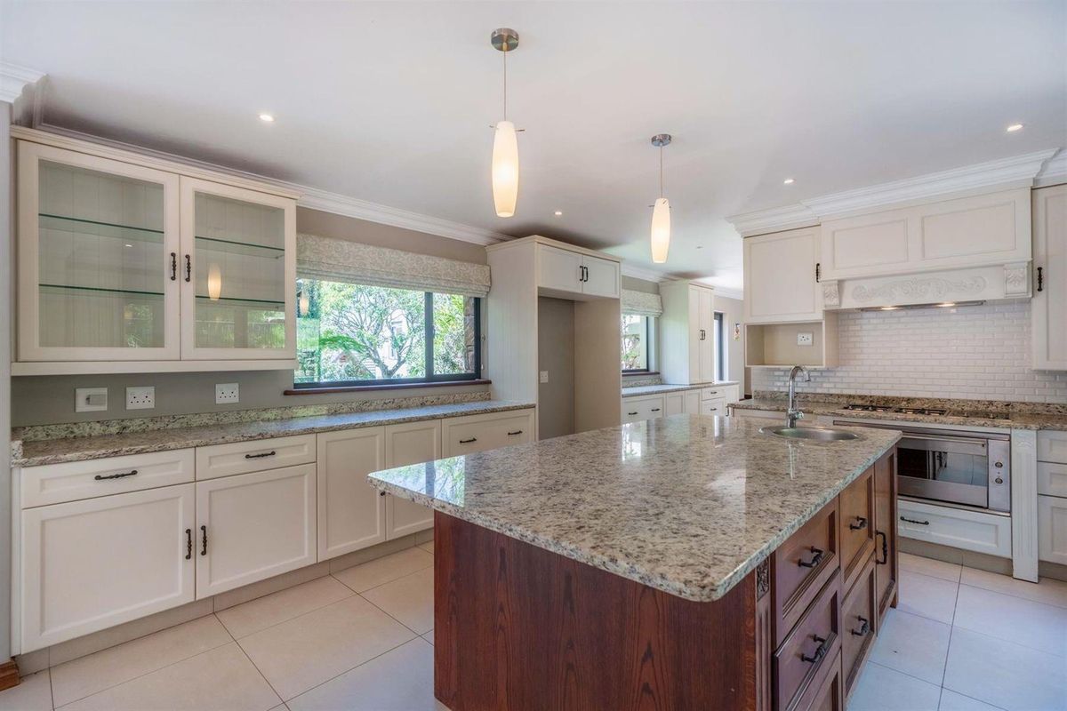 Spacious kitchen featuring granite countertops, a central island with storage, built-in oven, gas hob, and classic cabinetry with glass-front display units.