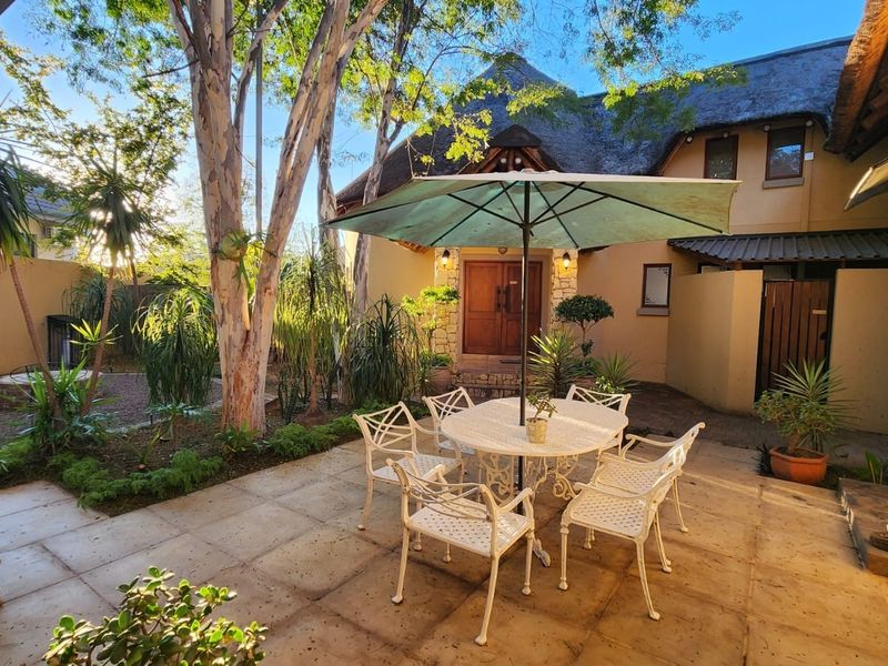 A charming outdoor patio area featuring paved flooring, stone accents, and a thatched roof entrance, providing a pleasant space for outdoor relaxation.