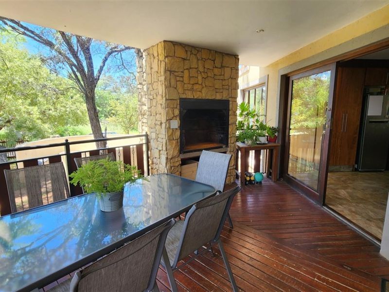 Covered patio featuring timber decking, a built-in stone-clad braai, and sliding door access to the interior living space.