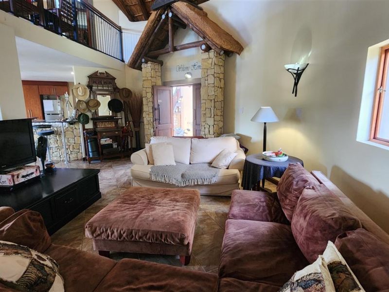 Spacious living area featuring a unique stone-clad entrance with a thatched roof detail, tiled flooring, and an open mezzanine level overlooking the space.