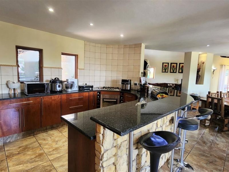 Open-plan kitchen featuring granite countertops, wooden cabinetry, a stone-clad breakfast bar, and tiled flooring, seamlessly flowing into the adjacent dining area.