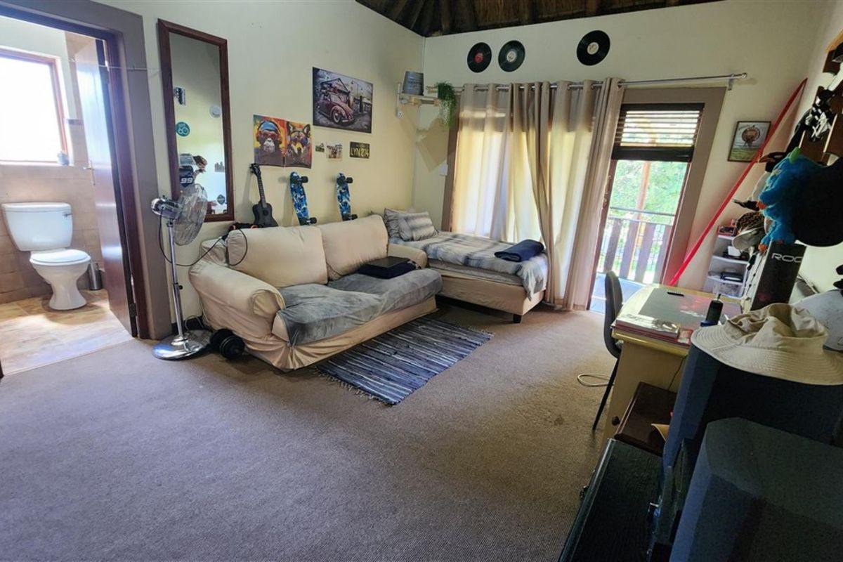A bedroom featuring a thatch ceiling, carpeted flooring, and an attached en-suite bathroom with a sliding door leading to an outdoor area.