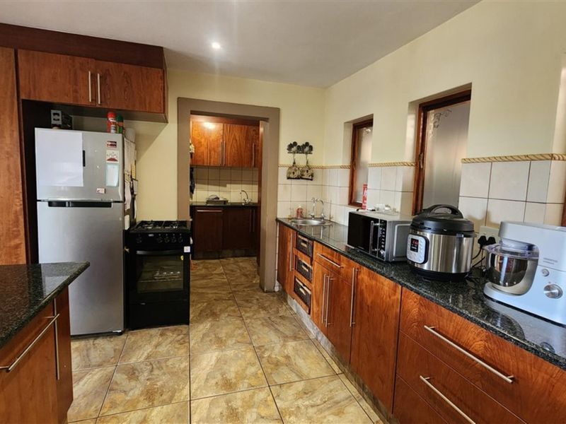 A functional kitchen featuring wooden cabinetry, granite countertops, tiled flooring, and a connected scullery area, providing ample storage and workspace.