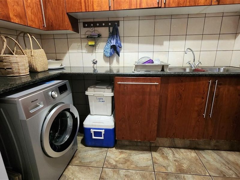 A functional laundry area featuring granite countertops, built-in wooden cabinetry, a stainless steel sink, and tiled flooring.