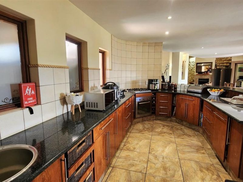 Spacious kitchen featuring wooden cabinetry, granite countertops, a built-in oven, gas hob, and tiled flooring, with an open-plan layout flowing into the living area.