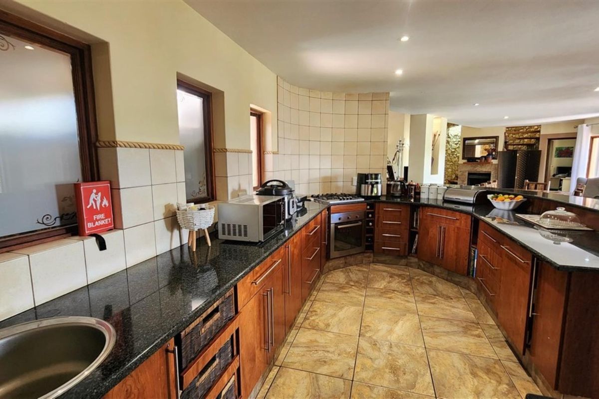 Spacious kitchen featuring wooden cabinetry, granite countertops, a built-in oven, gas hob, and tiled flooring, with an open-plan layout flowing into the living area.