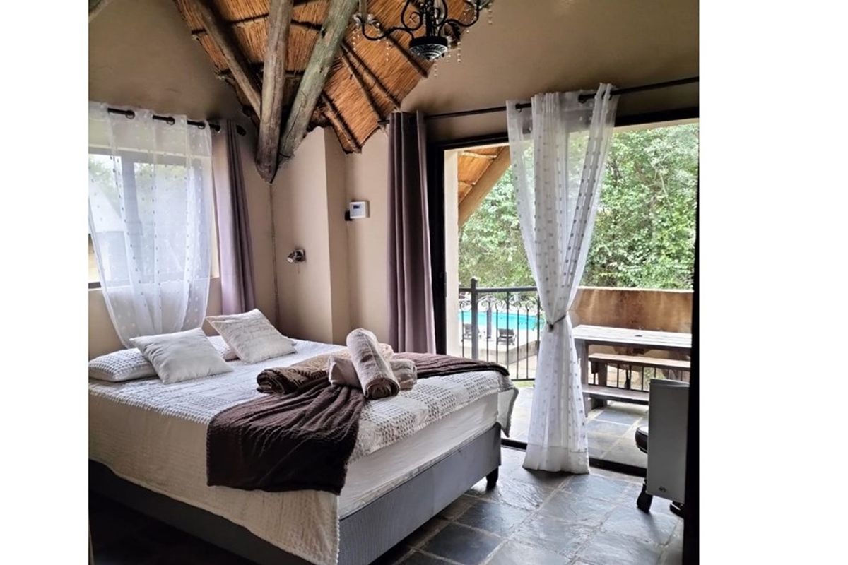 A cozy bedroom featuring a traditional thatched roof with exposed timber rafters, stone tile flooring, and direct access to a private balcony.