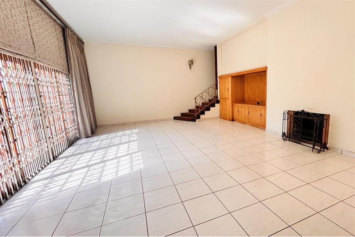 Spacious living area featuring tiled flooring, a built-in wooden cabinet, a fireplace, and a staircase leading to the upper level.