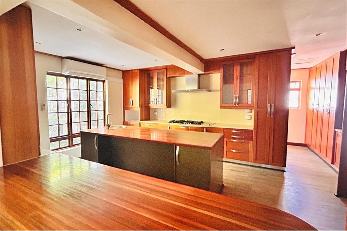 Spacious kitchen featuring warm wood cabinetry, a central island with a breakfast bar, built-in gas hob, extractor fan, and integrated storage solutions.