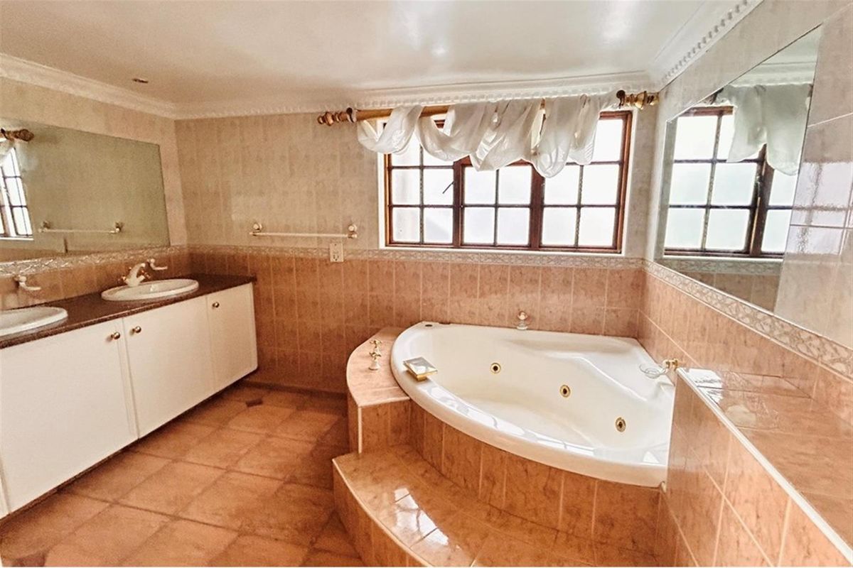 Spacious bathroom featuring a corner jetted tub, dual vanity with integrated sinks, and tiled wall and floor finishes.