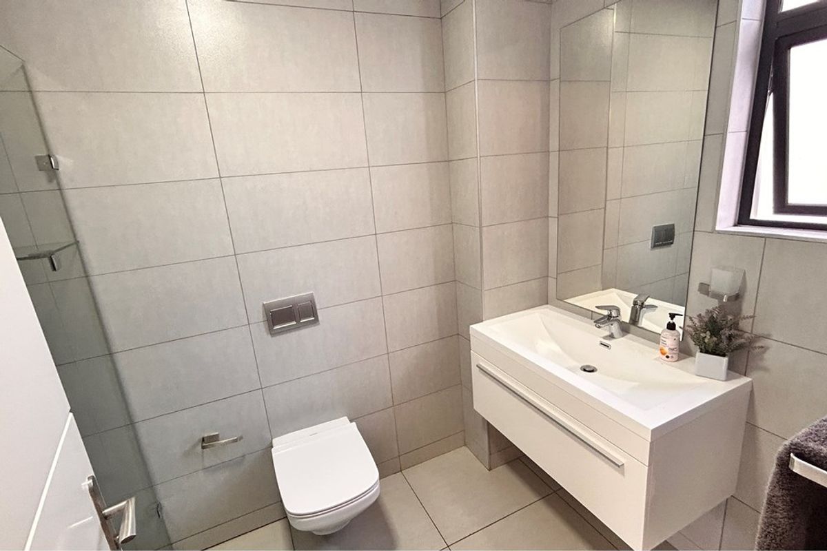 Modern bathroom featuring a wall-mounted toilet, floating vanity with integrated basin, large mirror, and neutral floor-to-ceiling tiling.