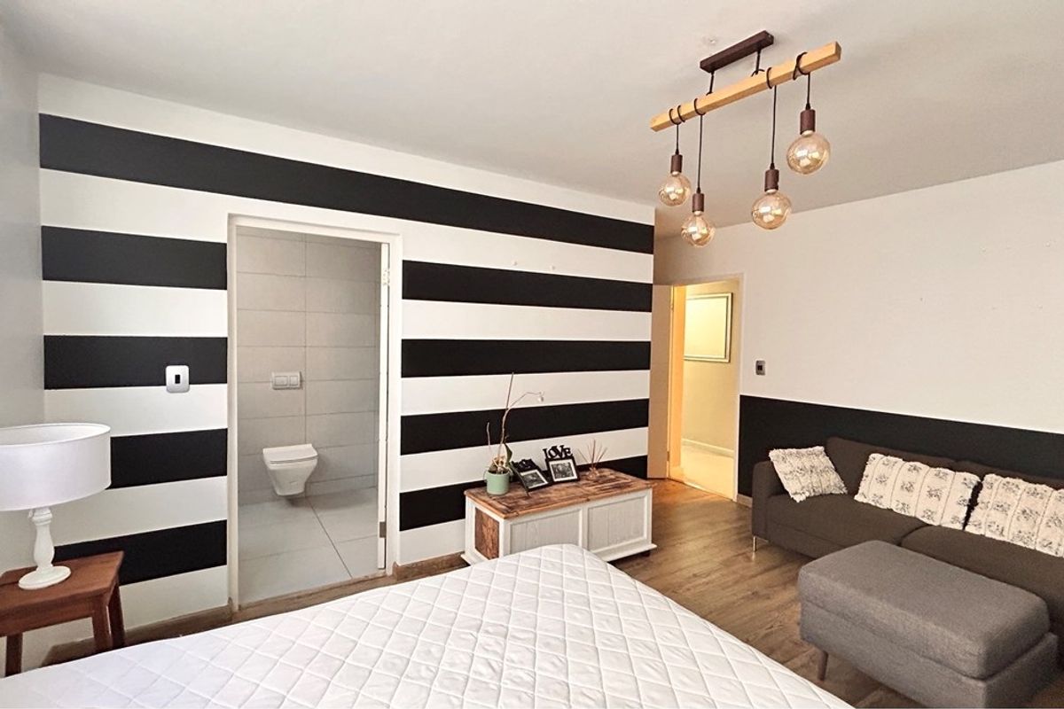 Bedroom featuring laminate flooring, modern pendant lighting, and direct access to an en-suite bathroom with tiled finishes.