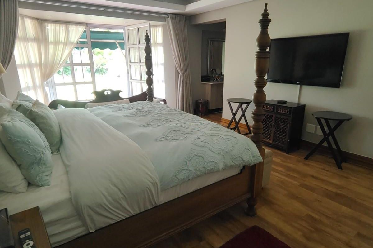 Spacious bedroom featuring hardwood flooring, a tray ceiling with recessed lighting, and direct access to an outdoor patio area.