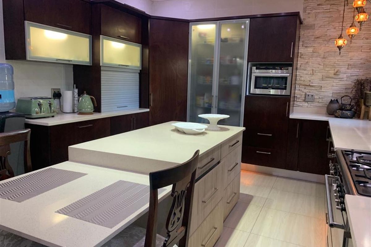 Modern kitchen featuring dark wood cabinetry, a central island with integrated seating, stone countertops, and a built-in oven.