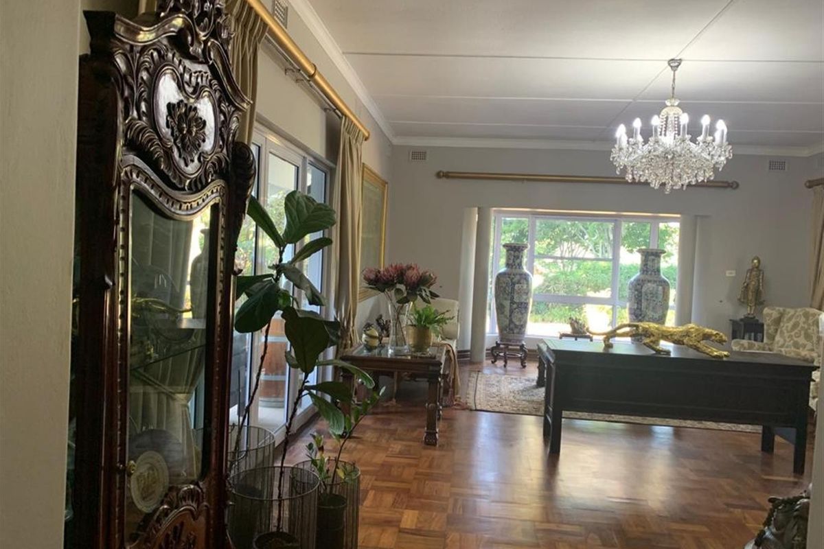 Spacious living room featuring classic parquet flooring, large windows providing natural light, and a decorative crystal chandelier.