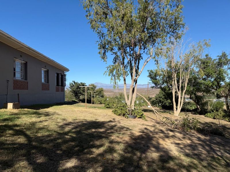 Rear view of the property showing the side facade, lawn area, and established trees with mountain views in the background.